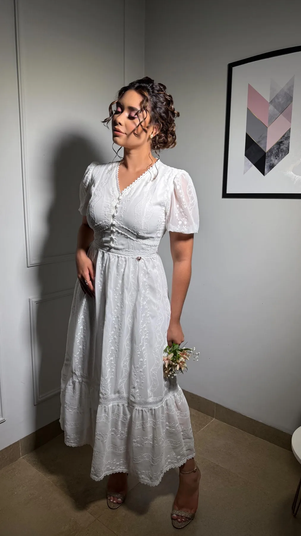 Mulher de cabelo preso usando o Vestido Camila branco bordado, com mangas bufantes, em um ambiente interno